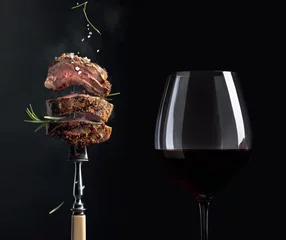 Poster Grilled  beef steak with rosemary and glass of red wine on a black background. © Igor Normann