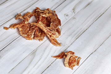 Dehydrated homemade chicken or turkey pet chips on white wooden background with big empty copy space for any text. Dog and cat chewy jerky and treats. Indoors, close up.