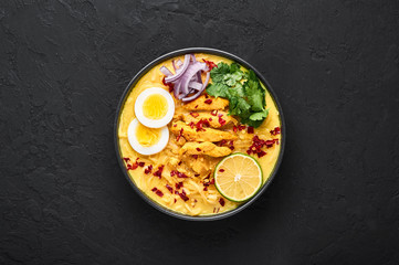 Ohn No Khao Swe in black bowl at dark slate background. Oh No Khao Suey is Coconut Milk Noodle Soup...