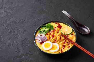 Ohn No Khao Swe in black bowl at dark slate background. Oh No Khao Suey is Coconut Milk Noodle Soup of myanmar cuisine with chicken meat and eggs. Burmese food. Copy space