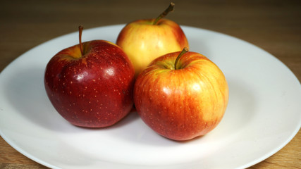 Ripe juicy red apple on a white ceramic plate on a table in the kitchen