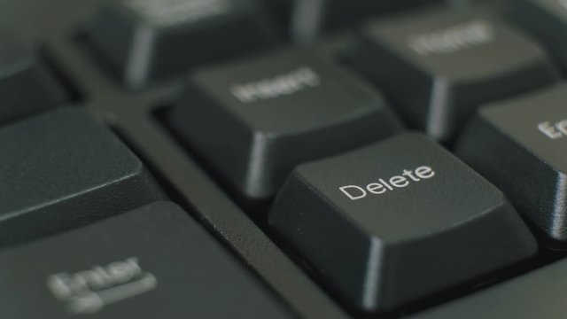 Finger repeatedly pressing the delete key on a black keyboard.