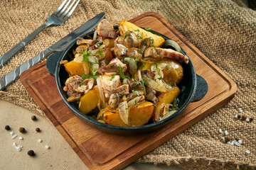 Dish in a pan - baked potatoes with onions, chicken and mushrooms on rustic background. Traditional Ukrainian dish. Close up view on food