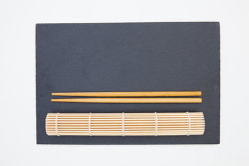 Rectangular slate plate with chopsticks, bamboo mat  for sushi on the white table.