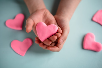 The child holds a plasticine heart in his hands. Love. Close up. Blue background. Concept for Valentine's Day and Mother's Day.