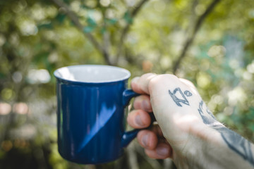 Holding blue metal cup with black coffee and coffee tattoo on wrist
