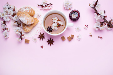 Cup of tea, croissants and spring twigs on a pink background. View from above