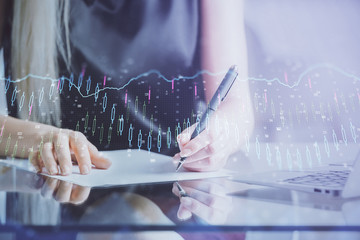 A woman hands writing information about stock market in notepad. Forex chart holograms in front. Concept of research.