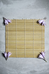 Spa concept. Bamboo mat, natural wooden matting, bass with flowers on the corner with space for text on cement grey background