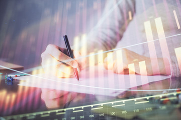 Hand taking notes in notepad. Forex chart holograms in front. Concept of research. Multi exposure