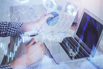 Double exposure of stock graph with businessman typing on computer in office on background. Concept of hard work.