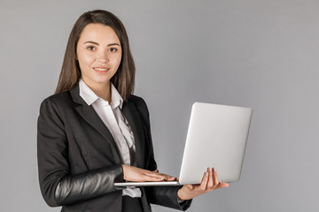 Young business woman in dark suite with laptop on grey background.