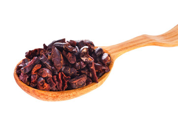 Cacao nibs in a wooden spoon isolated on a white background.