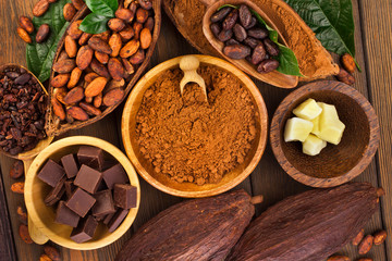 Cacao beans and powder, cacao butter and cacao nibs with chopped chocolate on a wooden background.