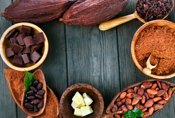 Cacao beans and powder, cacao butter and cacao nibs with chopped chocolate on a wooden background. Text space.