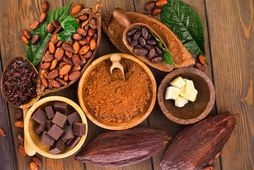 Cacao beans and powder, cacao butter and cacao nibs with chopped chocolate on a wooden background.