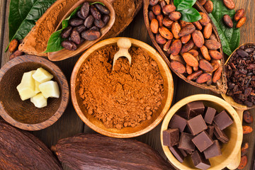 Cacao beans and powder, cacao butter and cacao nibs with chopped chocolate on a wooden background.