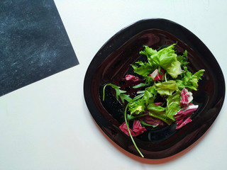 Black plate with vibrant lettuce leaves and greens on a white wooden table with a piece of  black napkin