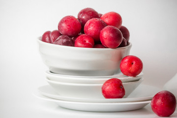 Many bright plums in the bowl on the table. Still life food. Light white kitchen. Organic healthy vegetarian food concept.