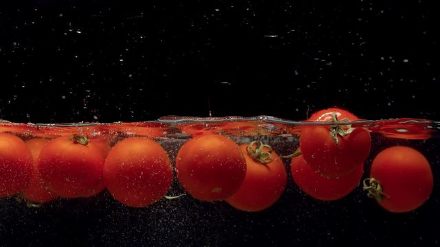 Close up tomatoes falling into the water with a splash and bubbles on black background