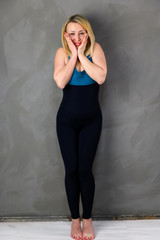 The concept of one fitness. Full-length photo of a pretty slender blonde woman athlete in a tracksuit on a gray background. Standing in different poses with emotions and a smile.