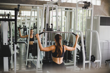 Fototapeta na wymiar Beautiful athlete exercising with a lat pulldown machine to play the arms and shoulder muscles in the gym.