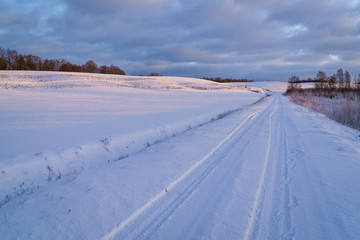 Fototapeta na wymiar Winter morning, country road and fields covered with snow, in the distance you can see a hilly landscape.