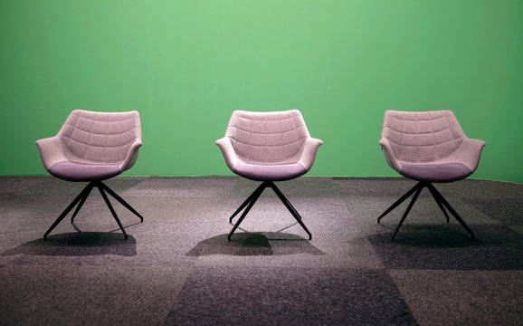 Three empty chairs in a TV studio with green screen background