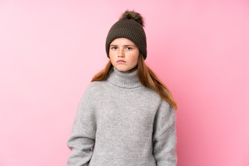 Ukrainian teenager girl with winter hat over isolated pink background sad