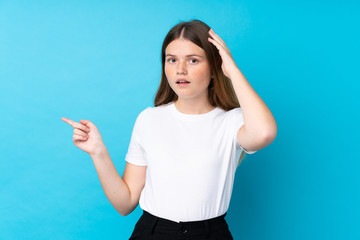 Ukrainian teenager girl over isolated blue background surprised and pointing finger to the side