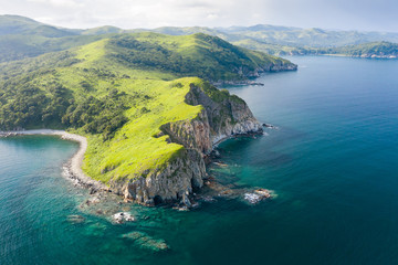 Aerial view of green rocky coastline and clean turquoise sea in Asia.  Cape Azaryev at Gamov Peninsula in summertime. Seaside nature landscape in Primorsky Krai, Far East, Russia