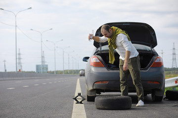 Replacing the wheel of a car on the road. A man doing tire work on the sidelines.