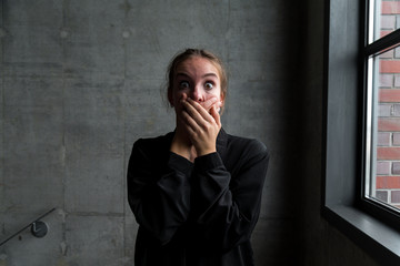 Young Woman with Shocked Facial Expression Covering Mouth with Hands