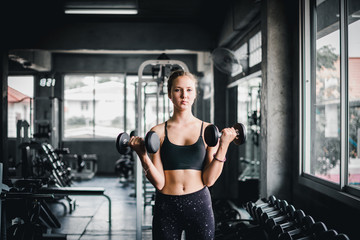 Naklejka na ściany i meble Beautiful female athletes are exercising in the gym. By lifting the dumbbell. The gym has a full range of exercise equipment.