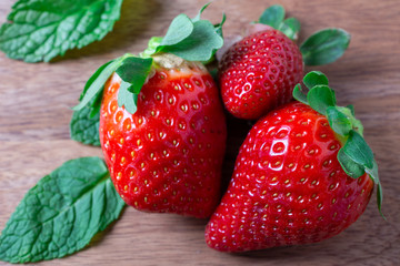 Close-up of three strawberries and mint leaves on wooden board, horizontally with space for text