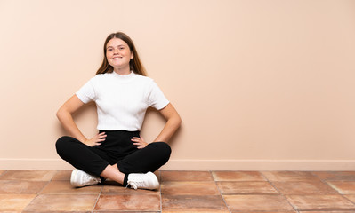 Fototapeta na wymiar Ukrainian teenager girl sitting on the floor posing with arms at hip and smiling