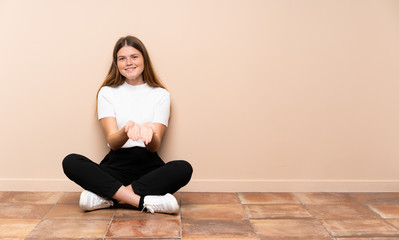 Ukrainian teenager girl sitting on the floor holding copyspace imaginary on the palm to insert an ad
