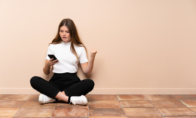Fototapeta na wymiar Ukrainian teenager girl sitting on the floor surprised and sending a message