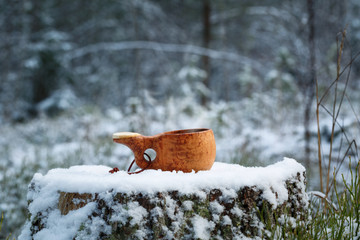 A wooden cup with tasty coffee stands on a stump in the winter forest.