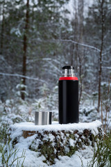 Thermos stands on an old stump in the forest. The background of the forest is blurred.