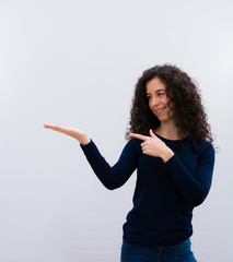 young pretty woman with black curly hair smiling, feeling happy, carefree and satisfied, pointing to concept or idea on copy space on the side against white wall.