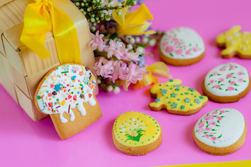 Flat lay Easter treats gingerbread cookies in the form of Easter cake, Easter eggs and rabbits decorated with glaze with spring flowers on a pink background with place for text