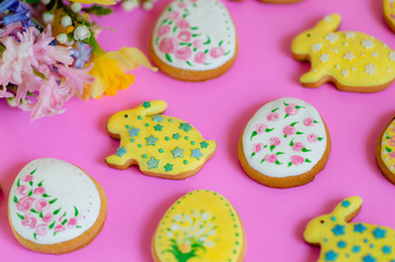 Flat lay of spring flowers and Easter ginger cookies in the shape of eggs and bunnies on a pink background.Happy Easter.Multi-colored pastel easter cookies on a pink background.Easter concept