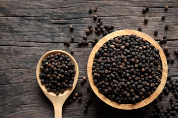 Black pepper seeds in a cup placed on old wooden table.