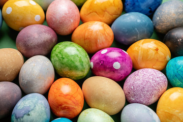 Different easter eggs with straw on wooden plate on green table