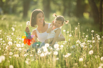 Portrait of happy mother and her little child on spring background. Cheerful family at dandelion field.Mom and her cute daughter outdoors.
