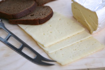 Black bread, different varieties of cheese and tomato on the board ready to eat