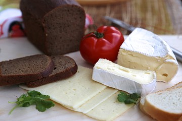 Black bread, different varieties of cheese and tomato on the board ready to eat