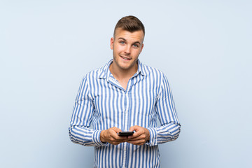 Young handsome blonde man over isolated blue background sending a message with the mobile