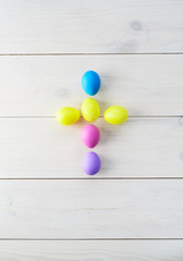 Easter eggs in the form of a cross on a light wooden background. Vertical orientation, top view.